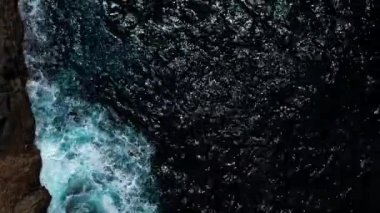 Derin mavi suyun üzerinde uçan İHA 'nın yukarıdan aşağı görüntüsü. Güçlü dalgalar Fuerteventura adasındaki siyah volkanik kayalara çarpıyor ve köpürüyor. Seyahat ve tatil kavramı.