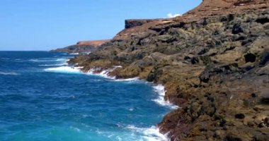 Güçlü dalgalar Fuerteventura adasındaki siyah volkanik kayalara çarpıyor ve köpürüyor. Seyahat ve tatil kavramı.
