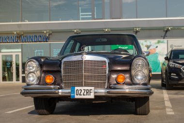 Klasik Mercedes-Benz 280 SE 1970 Tallinn City 'de güneşli bir yaz akşamında park edilmiştir. Modern şehir arka planında klasik araba. 