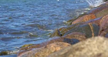 Deniz dalgalarının yakın çekimi sahildeki taşları eğlenceli bir şekilde okşuyor. Su ve toprağın büyüleyici dansı, detaylarıyla kaydedildi.