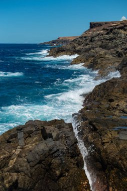 Derin mavi suyu olan güzel bir manzara. Güçlü dalgalar Fuerteventura adası Aguas Verdes sahilindeki siyah volkanik kayalara çarpar..