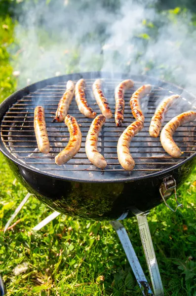 stock image Sizzling Sausages on Outdoor Barbecue Grill. Smoky Bratwurst Cooking Over Charcoal in Sunny Backyard