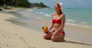 Kırmızı Bikini 'li kadın Mauritius Adası' nda Hindistan cevizi içeceğiyle plajda dinleniyor.