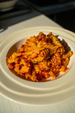 Jambon ve Fusilli, domates soslu. Beyaz tabakta servis edilen tuzlu İtalyan yemeği. Lezzetli Makarna Yemekleri 'nin yakın çekimi.