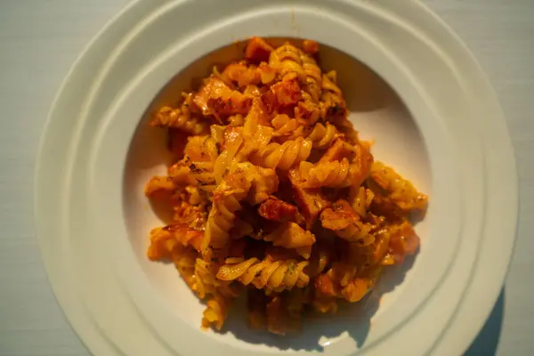Jambon ve Fusilli, domates soslu. Beyaz tabakta servis edilen tuzlu İtalyan yemeği. Lezzetli Makarna Yemekleri 'nin yakın çekimi.