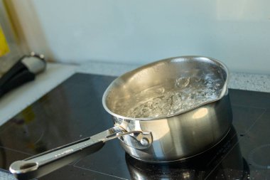 Paslanmaz çelik tencerenin tepesinde güçlü kaynar su bulunmakta. Profesyonel yemek takımı, kabarcıklar ve buharla aktif kaynadığını gösteriyor