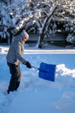 Kış mevsiminde Arka Bahçe Yolu 'ndan Kıdemli Kadın Karı Temizliyor. Kış mevsiminde araziyi karla kaplı ağaçlarla geçindiren yaşlı kişi