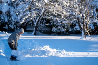 Kış mevsiminde Arka Bahçe Yolu 'ndan Kıdemli Kadın Karı Temizliyor. Kış mevsiminde araziyi karla kaplı ağaçlarla geçindiren yaşlı kişi