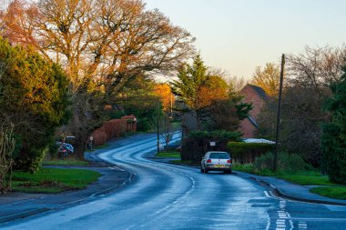 Takeley, İngiltere - 07 Aralık 2024: Kış Akşamı Virajlı Kırsal Yolu, Takeley Village, Essex. İngiliz Kırsalındaki Çıplak Ağaçlar Arasında Altın Saat Işığıyla Islak Virajlı Sokak