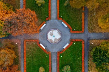 Merkezi çeşme plazası ve sonbahar renklerinin yer aldığı parkın kuş bakışı görüntüsü. Geometrik bahçe tasarımı, yeşil çimlere karşı turuncu ve sarı yapraklı mevsimsel geçişi vurguluyor