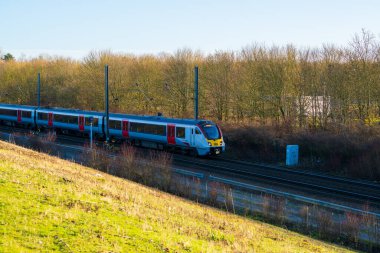 United Kingdom- 07 Aralık 2024: Essex, İngiltere 'deki Modern Greater Train on Railway Track during Winter Afternoon. Doğal Ormanlara Karşı Mavi ve Kırmızı Giyimli Yolcu Hizmeti Treni