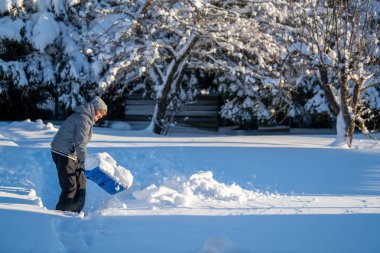 Kış mevsiminde Arka Bahçe Yolu 'ndan Kıdemli Kadın Karı Temizliyor. Kış mevsiminde karla kaplı ağaçlarla mülkün bakımını yapan yaşlı bir kişi