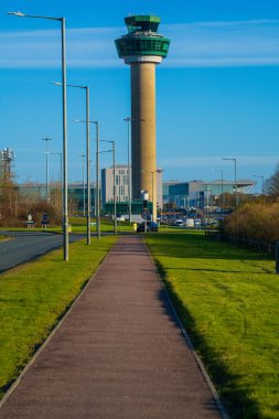 United Kingdom- 07 Aralık 2024: Modern Hava Trafik Kontrol Kulesi İngiltere Havaalanı. Açık mavi gökyüzü kendine özgü kontrol kulesini çerçevelerken havaalanı terminaline giden bir yol da...