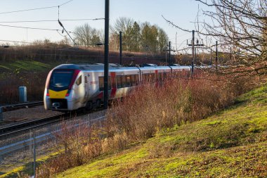 United Kingdom- 07 Aralık 2024: Essex, İngiltere 'deki Modern Greater Train on Railway Track during Winter Afternoon. Doğal Ormanlara Karşı Mavi ve Kırmızı Giyimli Yolcu Hizmeti Treni