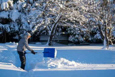 Kış mevsiminde Arka Bahçe Yolu 'ndan Kıdemli Kadın Karı Temizliyor. Kış mevsiminde karla kaplı ağaçlarla mülkün bakımını yapan yaşlı bir kişi