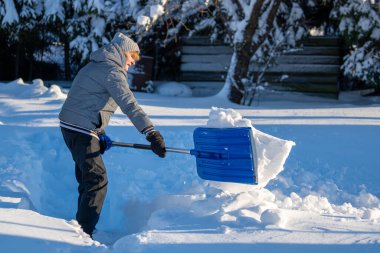 Kış mevsiminde Arka Bahçe Yolu 'ndan Kıdemli Kadın Karı Temizliyor. Kış mevsiminde karla kaplı ağaçlarla mülkün bakımını yapan yaşlı bir kişi
