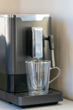 Süt köpüklü ve mutfak tezgahında çift duvarlı cam bardağı olan modern otomatik espresso makinesi. Pürüzsüz, buharlı kahve makinesi taze kapuçino ya da latte demlemek için hazırlandı.