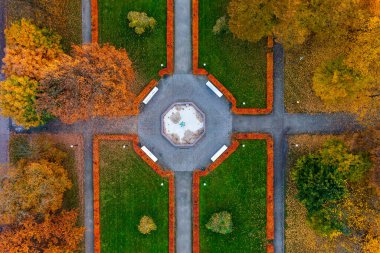 Merkezi çeşme plazası ve sonbahar renklerinin yer aldığı parkın kuş bakışı görüntüsü. Geometrik bahçe tasarımı, yeşil çimlere karşı turuncu ve sarı yapraklı mevsimsel geçişi vurguluyor
