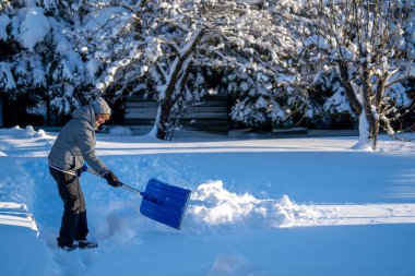 Kış mevsiminde Arka Bahçe Yolu 'ndan Kıdemli Kadın Karı Temizliyor. Kış mevsiminde karla kaplı ağaçlarla mülkün bakımını yapan yaşlı bir kişi