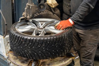 Garajdaki alüminyum tekerleğin üzerinde çivili bir kış lastiğinin profesyonel montajı. Özel ekipmanlı mevsimlik lastik değiştirme servisi.