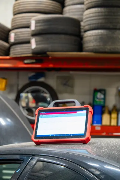 Dijital bir tanılama tableti, geniş bir lastik deposu olan bir oto tamirhanesinde bulunan bir araçta. Organize envanter sistemine sahip modern araba servisi atölyesinde kullanılan profesyonel otomotiv teşhis aracı