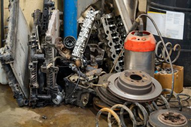 Garaj köşesinde fren diskleri, motor parçaları ve bobin yayları da dahil olmak üzere kullanılmış araç parçaları var. Otomotiv tamir atölyesi hurda metal koleksiyonu geri dönüşümü ya da imha edilmeyi bekleyen eski parçaları gösteriyor
