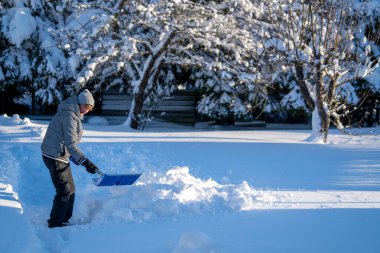 Kış mevsiminde Arka Bahçe Yolu 'ndan Kıdemli Kadın Karı Temizliyor. Kış mevsiminde karla kaplı ağaçlarla mülkün bakımını yapan yaşlı bir kişi