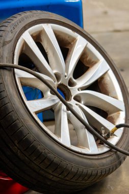 Hava basıncı hortumu, gümüş alaşım tekerindeki valf sapına bağlandı ve görünür fren tozu birikti. Otomotiv garajında mevsimsel tekerlek değiştirme sırasında lastik enflasyonu prosedürünün ayrıntılı görünümü