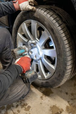 Siyah bir araç üzerinde çalışan bir otomotiv teknisyeniyle Mevsimlik Lastik Değiştirme Servisi. Yaz Tekerleği Kurulumu İçin Bir Darbe Anahtarı Kullanımı