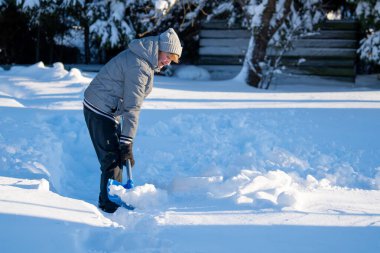 Kış mevsiminde Arka Bahçe Yolu 'ndan Kıdemli Kadın Karı Temizliyor. Kış mevsiminde karla kaplı ağaçlarla mülkün bakımını yapan yaşlı bir kişi