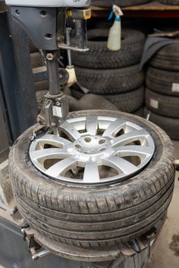 Lastik montaj makinesi, servis garajındaki gümüş alaşımlı bir tekerleğe yazlık lastik takıyor. Profesyonel ekipman mevsimsel lastik değişimi sırasında kurulumu tamamlar