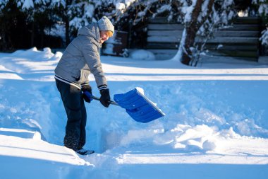 Kış mevsiminde Arka Bahçe Yolu 'ndan Kıdemli Kadın Karı Temizliyor. Kış mevsiminde karla kaplı ağaçlarla mülkün bakımını yapan yaşlı bir kişi