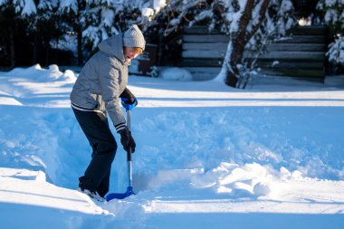 Kış mevsiminde Arka Bahçe Yolu 'ndan Kıdemli Kadın Karı Temizliyor. Kış mevsiminde karla kaplı ağaçlarla mülkün bakımını yapan yaşlı bir kişi