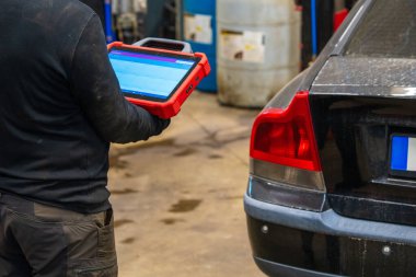 Otomotiv tamirhanesinde elektronik tablet tarayıcı kullanan bir araba teşhis uzmanı. Tamirci, profesyonel teşhis ekipmanlarıyla araç bilgisayar sistemi analizi yapıyor.