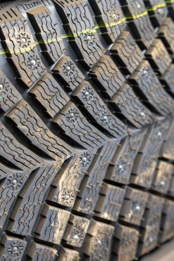 Premium çivili kış lastiklerinin detaylı bir görüntüsü saldırgan lastik izleri ve metal kavrama elementlerini gösteriyor. Aşırı soğuk hava sürüşü için yüksek performanslı kar lastiğinin yakın plan çekimi.