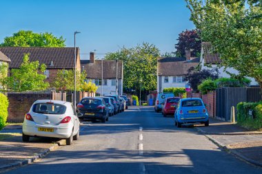 Norwich, UK- 17 Mayıs 2025 Norwich, İngiltere 'deki tuğla evlerin önüne park edilmiş arabalarla sakin bir banliyö sokak sahnesi. Karışık konutları ve yeşil peyzajı olan geleneksel İngiliz yerleşim yeri