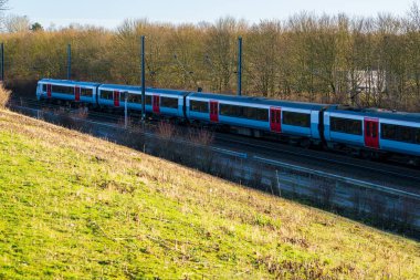 United Kingdom- 07 Aralık 2024: Essex, İngiltere 'deki Modern Greater Train on Railway Track during Winter Afternoon. Doğal Ormanlara Karşı Mavi ve Kırmızı Giyimli Yolcu Hizmeti Treni