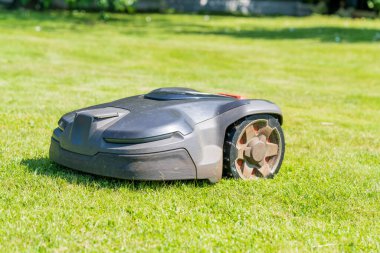 Robotik çim biçme makinesi otomatikman güneşli arka bahçedeki yeşil çimlerin çimlerini kesiyor. Modern akıllı bahçe teknolojisi cihazı konut bakımı üzerinde çalışıyor..
