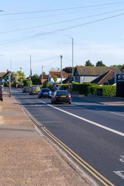 Norwich, UK- 17 Mayıs 2025: Norwich 'te evleri ve elektrik altyapısı olan bir yerleşim yolunda trafik akışı. Arabaların ve geleneksel mahalle binalarının yer aldığı İngiliz banliyö sokak sahnesi