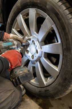 Mevsimlik lastik değiştirme işlemi, bir tamircinin, tekerlek cıvatalarını gevşetmek için ingiliz anahtarı kullandığını gösteriyor. Profesyonel otomotiv bakım ve onarım hizmeti