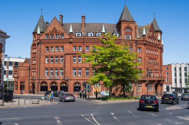 Norwich, UK- 17 Mayıs 2025: Norwich şehir merkezinde süslü kuleleri ve kuleleri olan Viktorya dönemi kırmızı tuğla binası. Meşgul bir caddede dekoratif taş işçiliğinin ve konik çatıların yer aldığı tarihi mimari