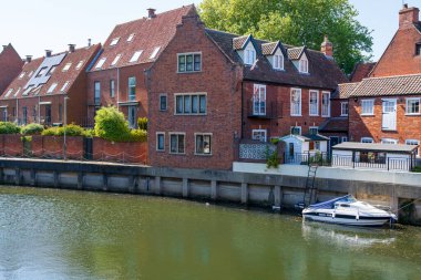 Norwich, UK- 17 Mayıs 2025: Geleneksel kırmızı tuğlalı nehir kenarlı evler Norwich, İngiltere 'de Wensum nehri boyunca demirli bir zevk teknesi ile. Tarihi İngiliz kenti rıhtım mimarisi ve kanal sahnesi.