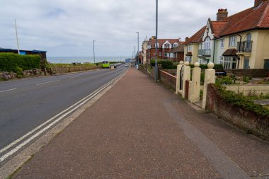 Cromer, UK- May 18, 2025: Coastal road and sidewalk along the seafront in Cromer, Norfolk, England, with traditional houses and ocean view on an overcast day