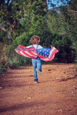 Kırsal kesimde yeşil ağaçlı ve renkli Amerikan bayrağıyla koşan kimliği belirsiz aktif çocuğun tüm vücudu.