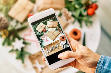 Kağıt Noel hediyelerine sarılı fotoğraf çeken tanınmayan insanların genel bakış açısı ladin dalları ve ipin yanında xmax ve baston şekerlemelerin yanında.