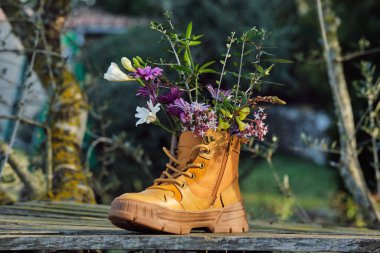 Banliyöde ağaç gövdeleri ve bulanık arka planda bina ile ahşap yüzeye yerleştirilmiş kahverengi çiçekli ayakkabılar.