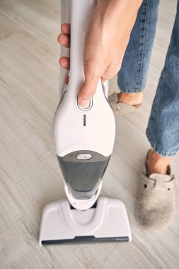 Sıradan giysiler içinde tanınmayan bir kadın. Evdeki rutin ev işleri sırasında plastik konteynırı modern dik elektrik süpürgesinden temizliyor.