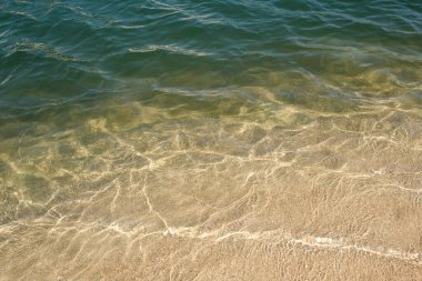 Şeffaf, dalgalanan temiz deniz suyunun tam çerçeve arka planı ıslak kumlu kıyıları yıkıyor.