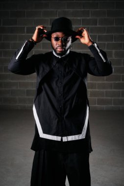 Siyah elbiseli ve güneş gözlüklü ciddi bir adam karanlık odada kameraya bakarken...