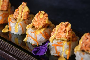 Somon ve taze sosla kaplı iştah açıcı suşinin yukarısından restorandaki ahşap tabakta servis edilen siyah arka plana karşı.